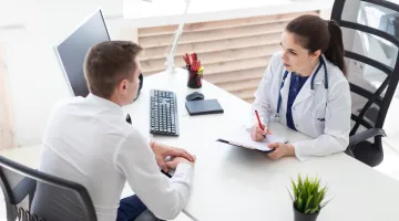 A woman doctor sits at a desk with a patient discussing his care